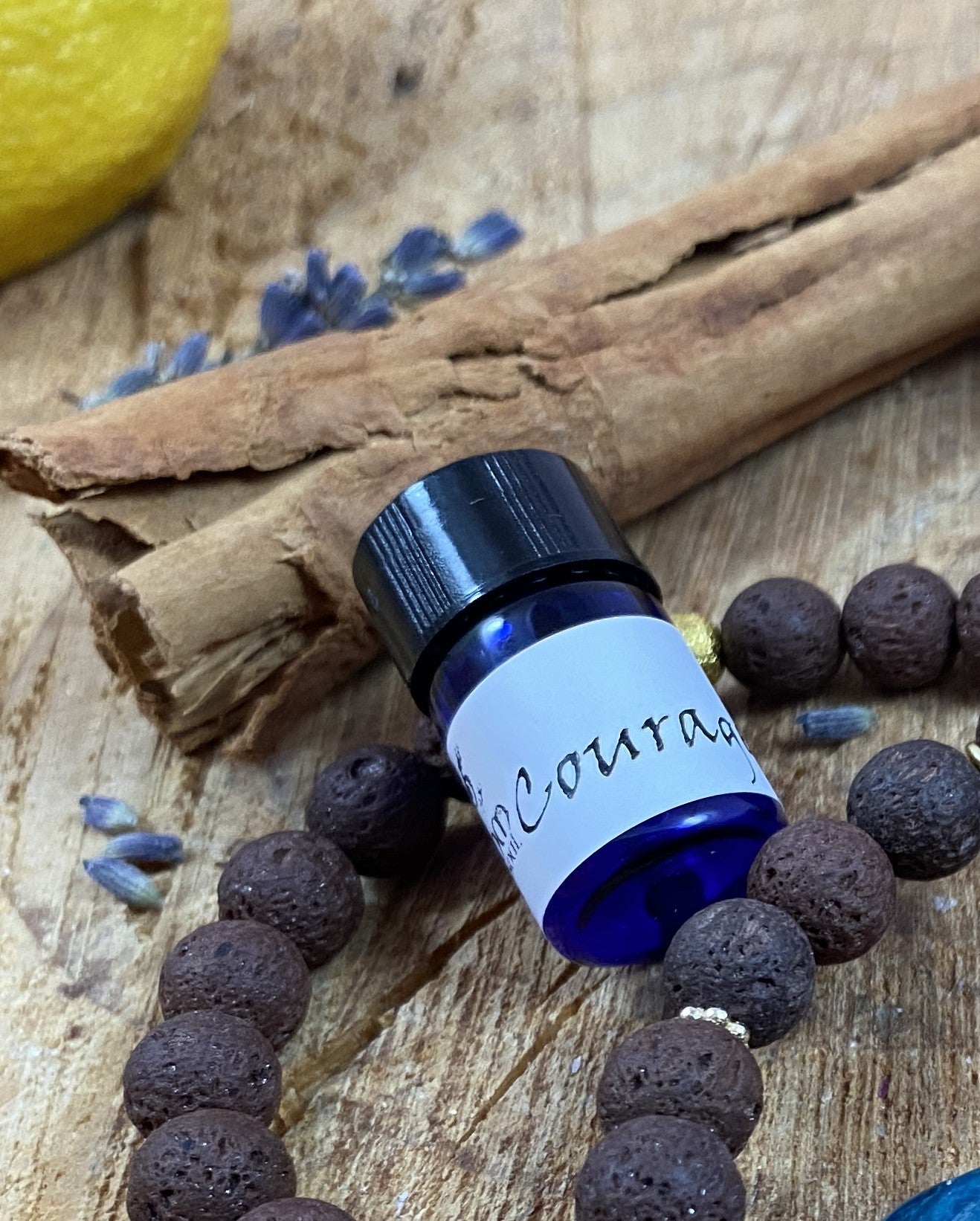 Small blue bottle labeled 'Courage' on a wooden surface with cinnamon sticks and lavender.