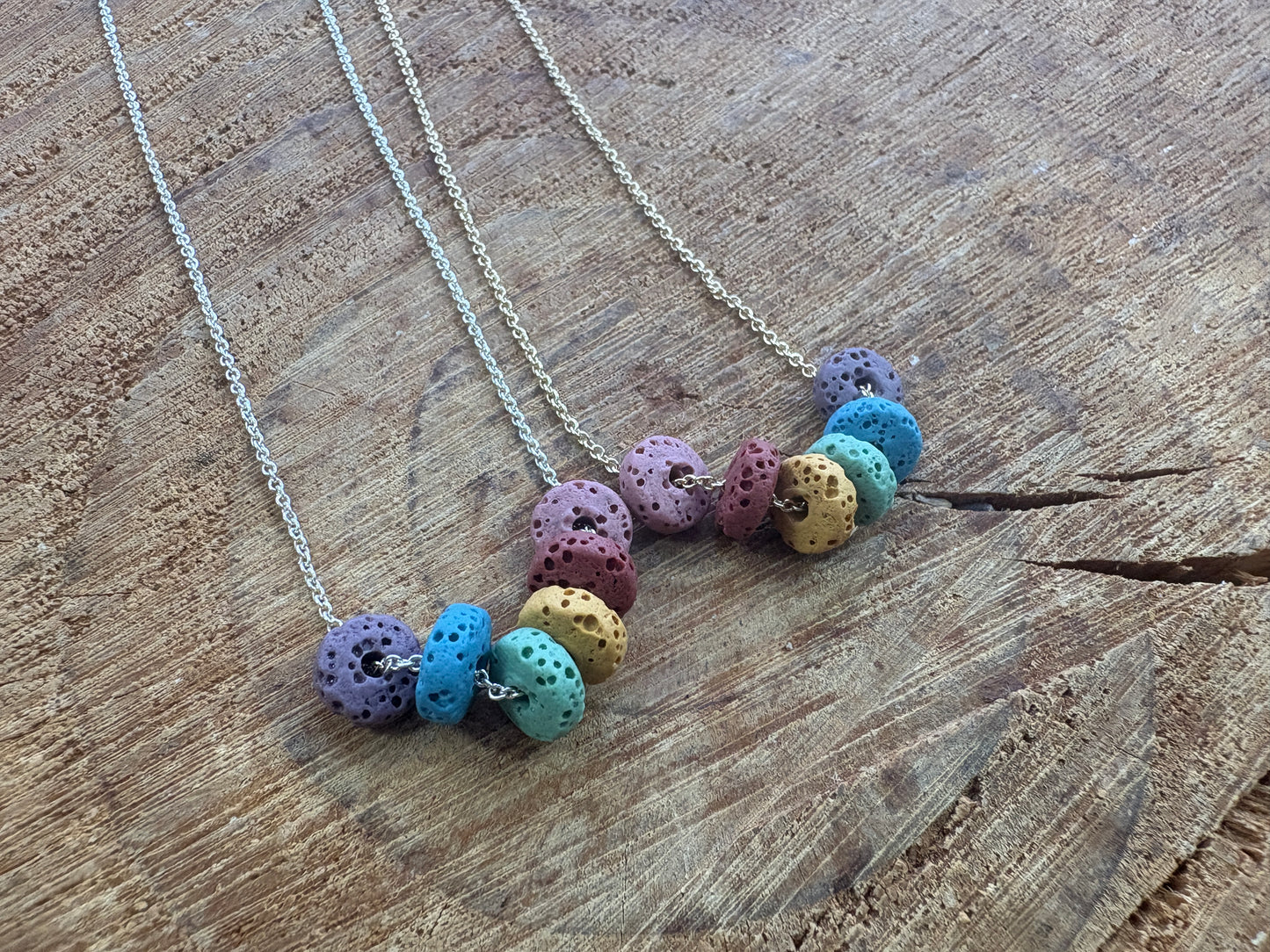 Two chain necklaces with clusters of colorful lava beads, displayed on a rustic wooden surface.