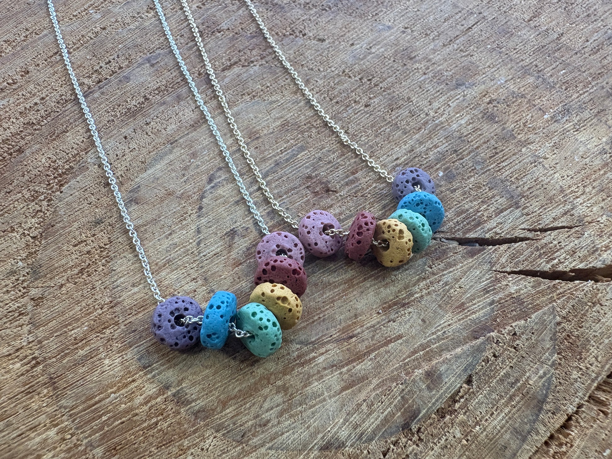 Two chain necklaces with clusters of colorful lava beads, displayed on a rustic wooden surface.
